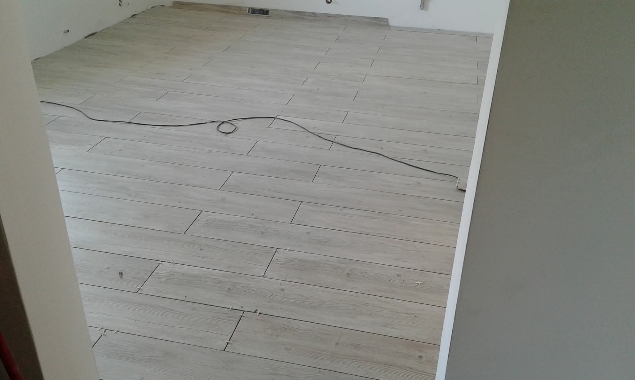 Ułożona podłoga z płytek imitujących drewno w Wyszkowie. Widoczne krzyżyki dystansowe i kabel. Jasne płytki ułożone w regularny wzór, świeżo po montażu.