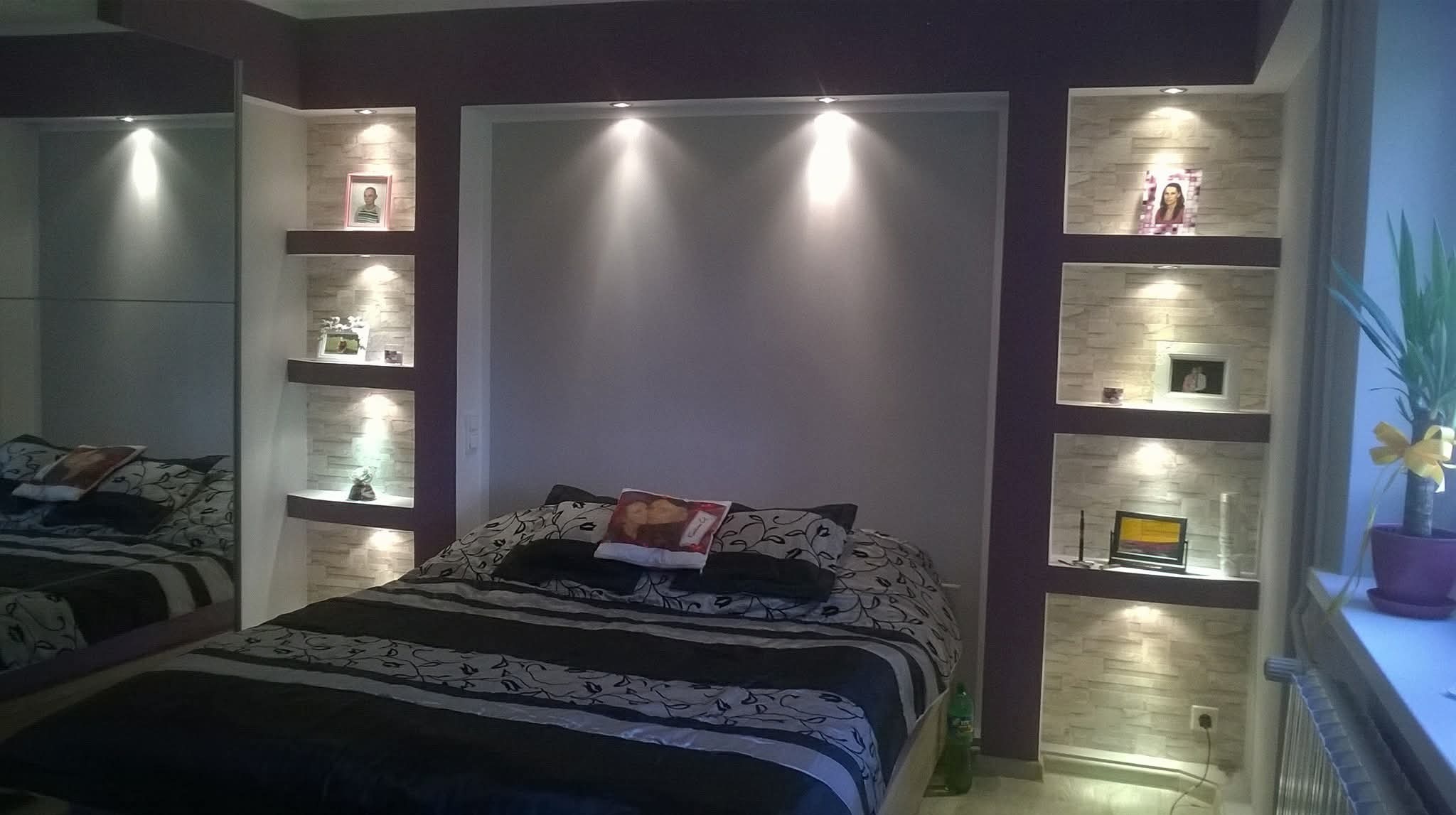 Sypialnia z wnękami wykończonymi dekoracyjną cegłą i oświetleniem punktowym. Ciemna kolorystyka ścian i mebli. Lustrzana szafa po lewej stronie.