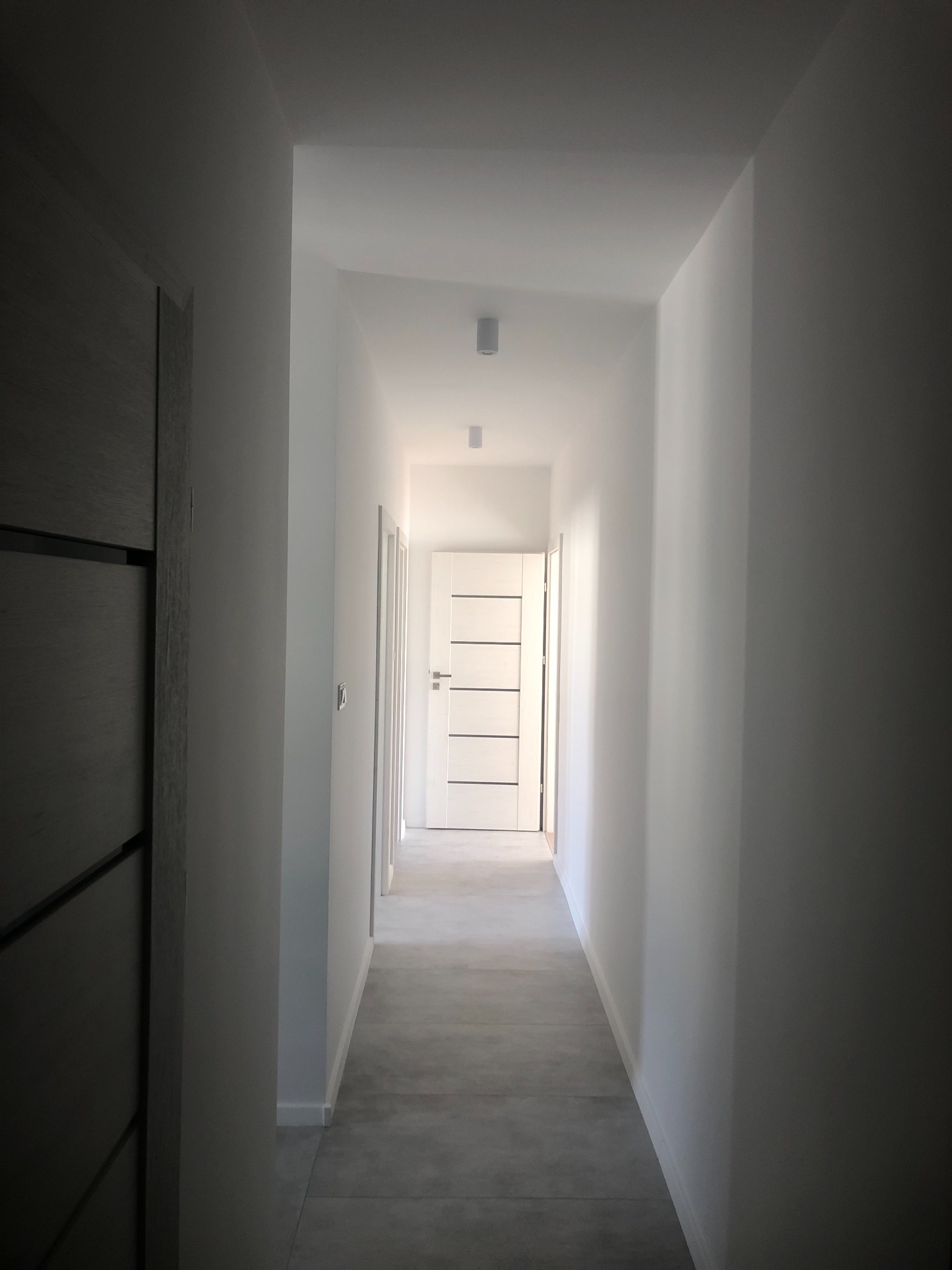 Jasny korytarz w odcieniach szarości i bieli, z widocznymi drzwiami po obu stronach, świeżo po remoncie.