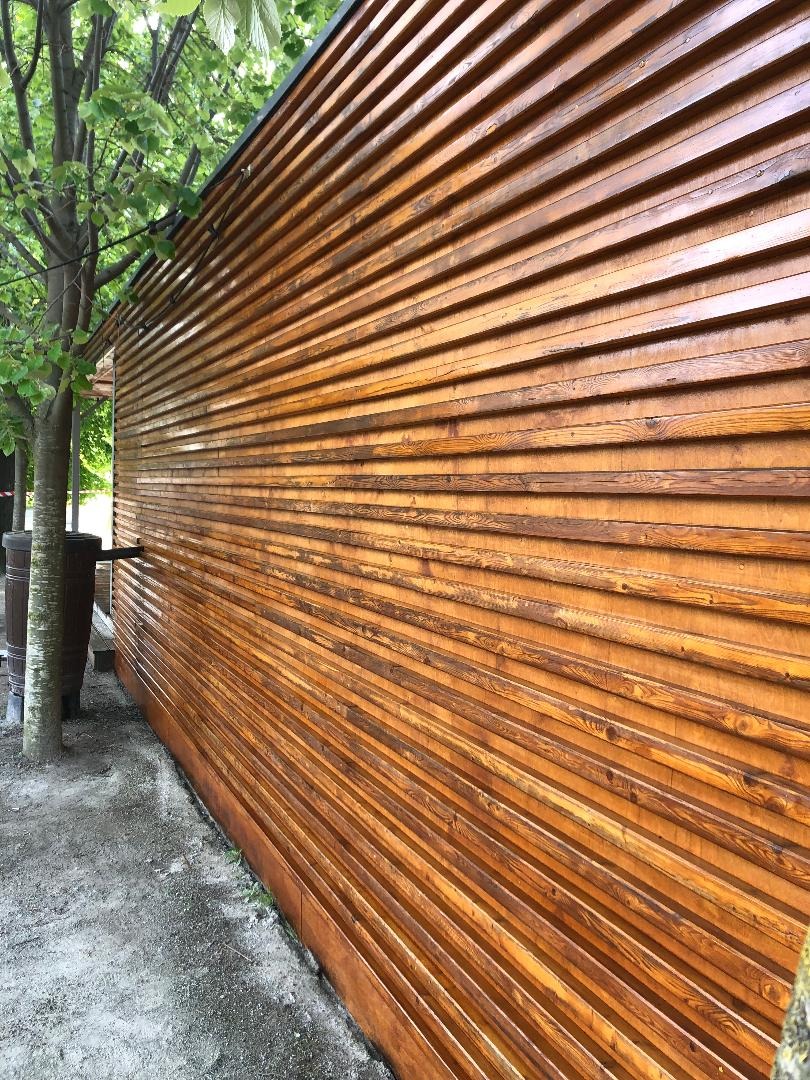 Świeżo polakierowana, drewniana elewacja budynku z widoczną strukturą drewna i cieniem drzewa