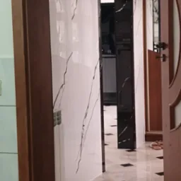 Wykończona ściana z białych płytek imitujących marmur z czarnymi żyłami, czarna rama drzwi i podłoga z jasnych płytek z czarnymi wstawkami, widok na wnętrze mieszkania.