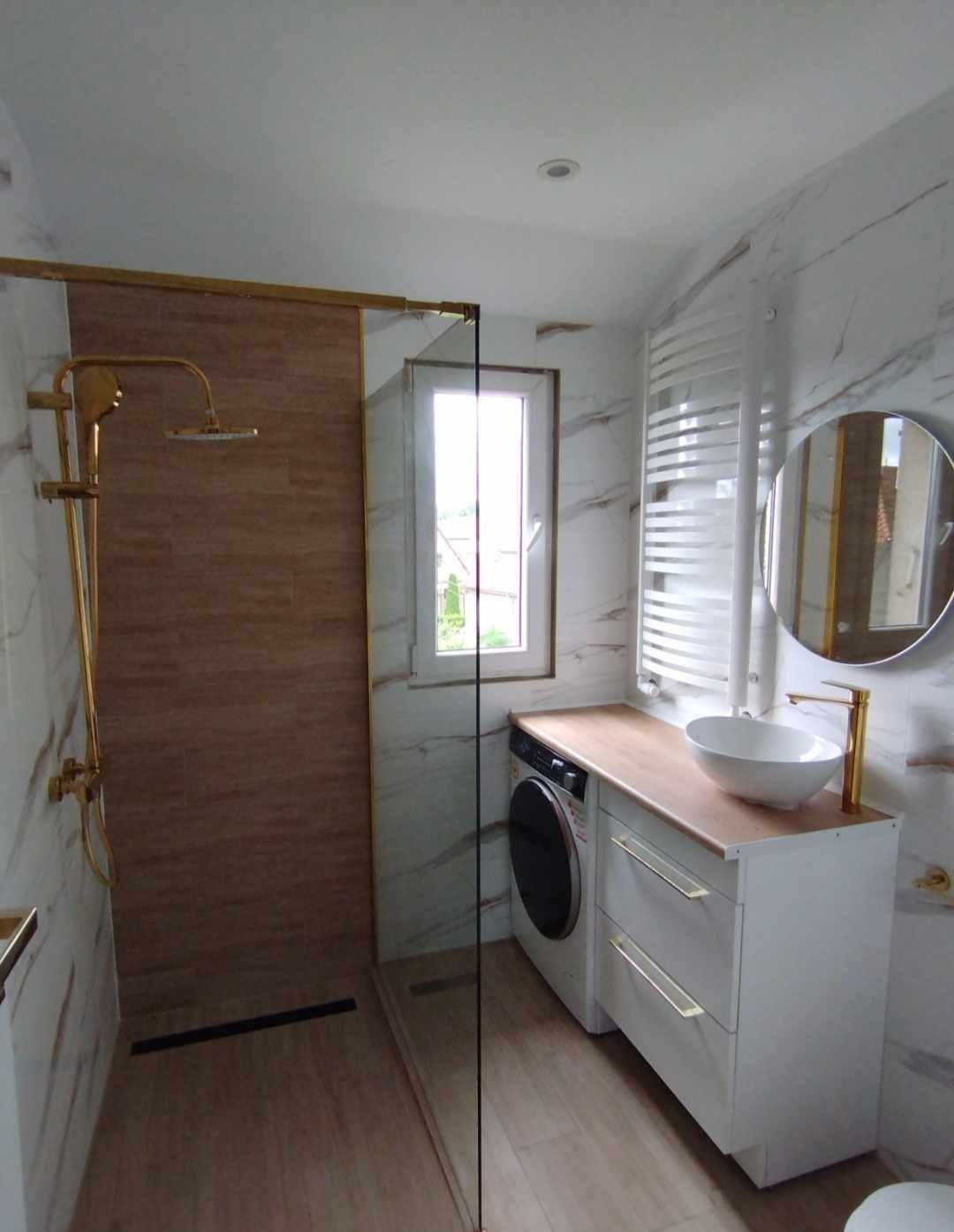 Nowoczesna łazienka z kabiną prysznicową typu walk-in, złotą armaturą, umywalką nablatową i pralką w zabudowie pod blatem.