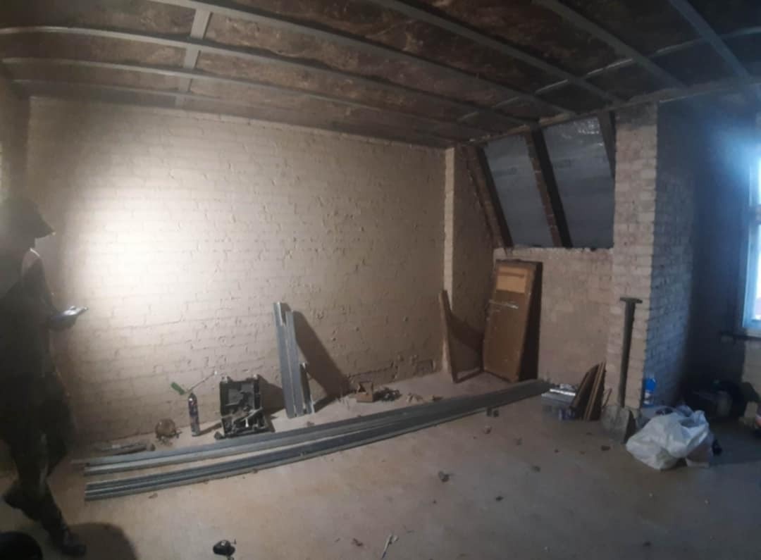 Poddasze w trakcie ocieplania: widoczne profile metalowe na suficie, częściowo ocieplone ściany, narzędzia i materiały budowlane rozłożone na podłodze, fragment okna po prawej.