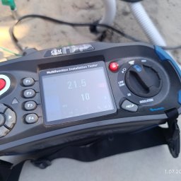 Radosław Kwiatkowski Instalacje - Miernik instalacji elektrycznej CEM DT-6650 z widocznymi wynikami pomiarów (21.5 Ω, 10 A, 50 V) na ekranie, podłączony do przewodów na betonowym podłożu.