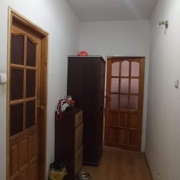 USŁUGI REMONTOWO-WYKOŃCZENIOWE Tomasz Florkowski - Korytarz po remoncie z drewnianą podłogą, dwojgiem drewnianych drzwi z przeszkleniami, ciemną szafą i komodą, widoczne miski dla zwierząt i torba na śmieci.