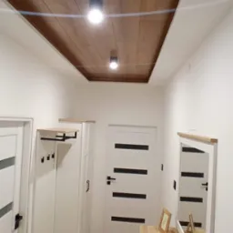 Nowoczesny przedpok&oacute;j z drewnianym sufitem podwieszanym z oświetleniem punktowym, białymi ścianami, panelami podłogowymi, szafą z wieszakiem, komodą z lustrem i dekoracjami.