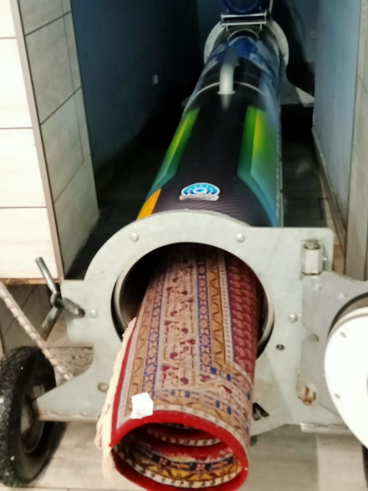 Orientalny dywan wkładany do specjalistycznej maszyny czyszczącej w Kostrzynie nad Odrą, widoczne detale wzoru i mocna, czerwona bordiura.