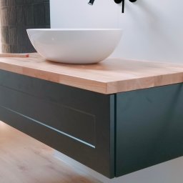 MebleRafi - Nowoczesna łazienka z wiszącą szafką pod umywalkę z blatem z jasnego drewna, okrągła biała umywalka nablatowa, czarna bateria i linijka stolarska na blacie.