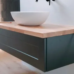 Nowoczesna łazienka z wiszącą szafką pod umywalkę z blatem z jasnego drewna, okrągła biała umywalka nablatowa, czarna bateria i linijka stolarska na blacie.