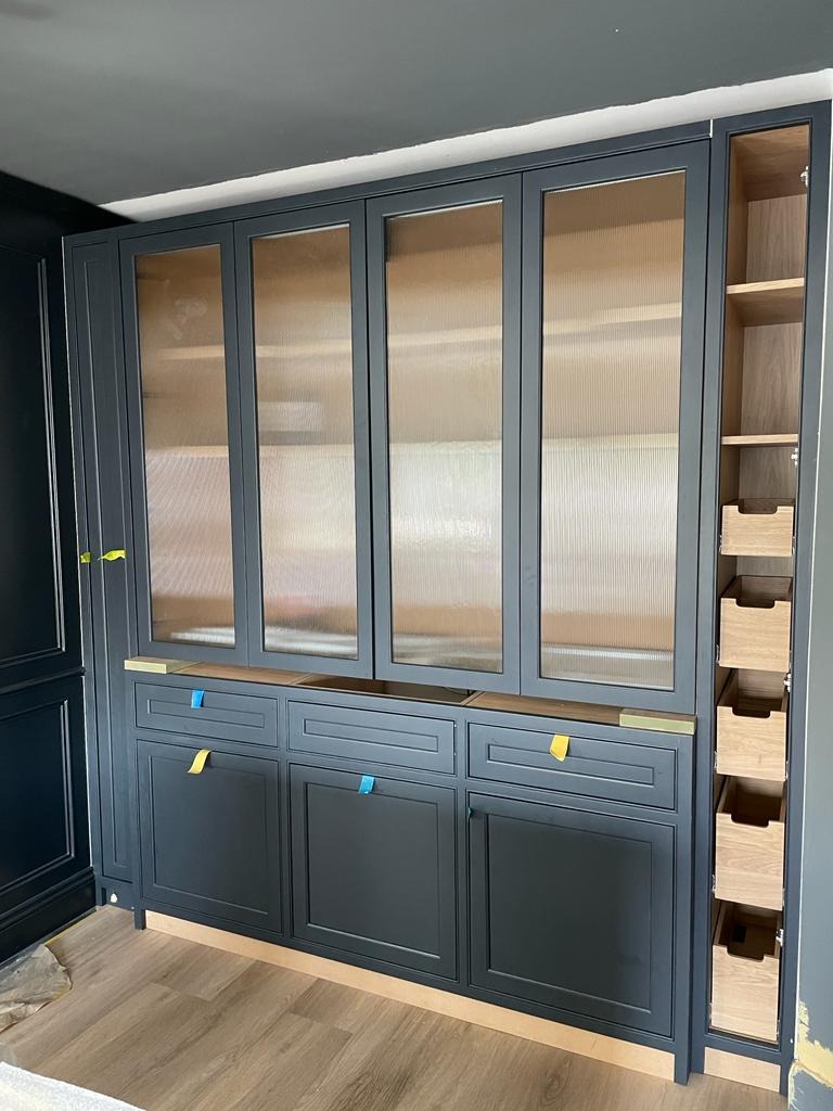 Ciemnoszara zabudowa kuchenna z ryflowanymi szklanymi frontami szafek górnych i szufladami dolnymi, widoczne drewniane kosze cargo w szafce bocznej, zabezpieczenia na szufladach, podłoga...