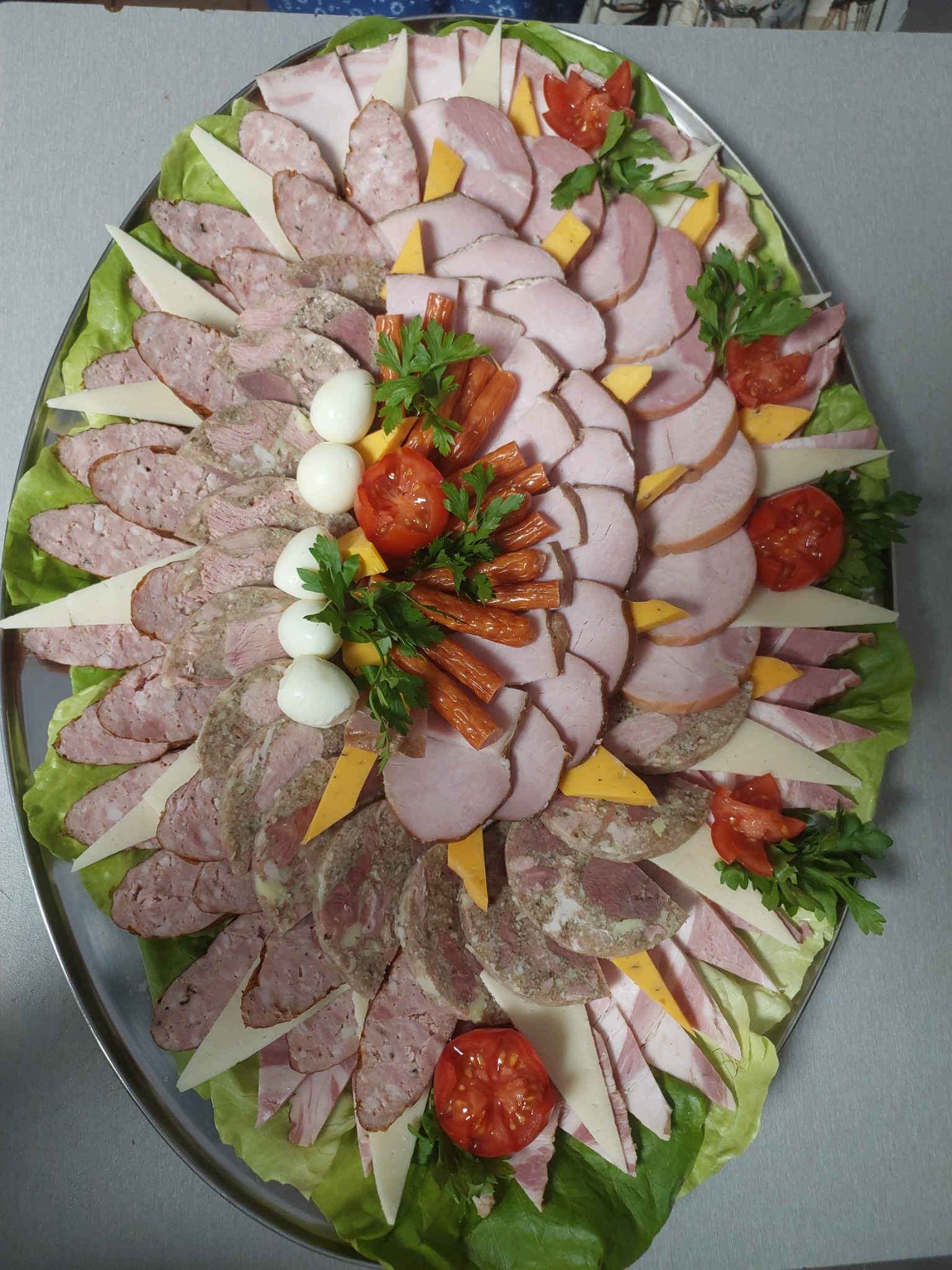 Dekoracyjna taca z wędlinami, serami i jajkami przepiórczymi, udekorowana sałatą i pomidorami koktajlowymi, tworząca apetyczną kompozycję.
