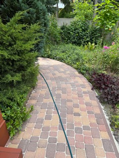 Nowy chodnik chodnika wyłożonego w okół domu z kostki betonowej po czyszczeniu ciśnieniowym oraz uzupełnieniu ubytków.