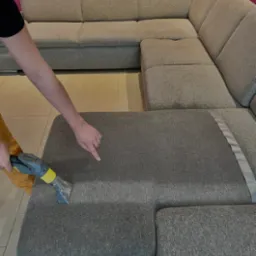 Czyszczenie narożnika z szarej tkaniny za pomocą odkurzacza piorącego, widoczna mokra plama po czyszczeniu, wskazująca na skuteczność działania.