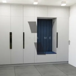 Biała szafa wnękowa z siedziskiem obitym granatowym materiałem, podświetlona sufitowymi lampami, z długimi, pionowymi, lustrzanymi uchwytami.