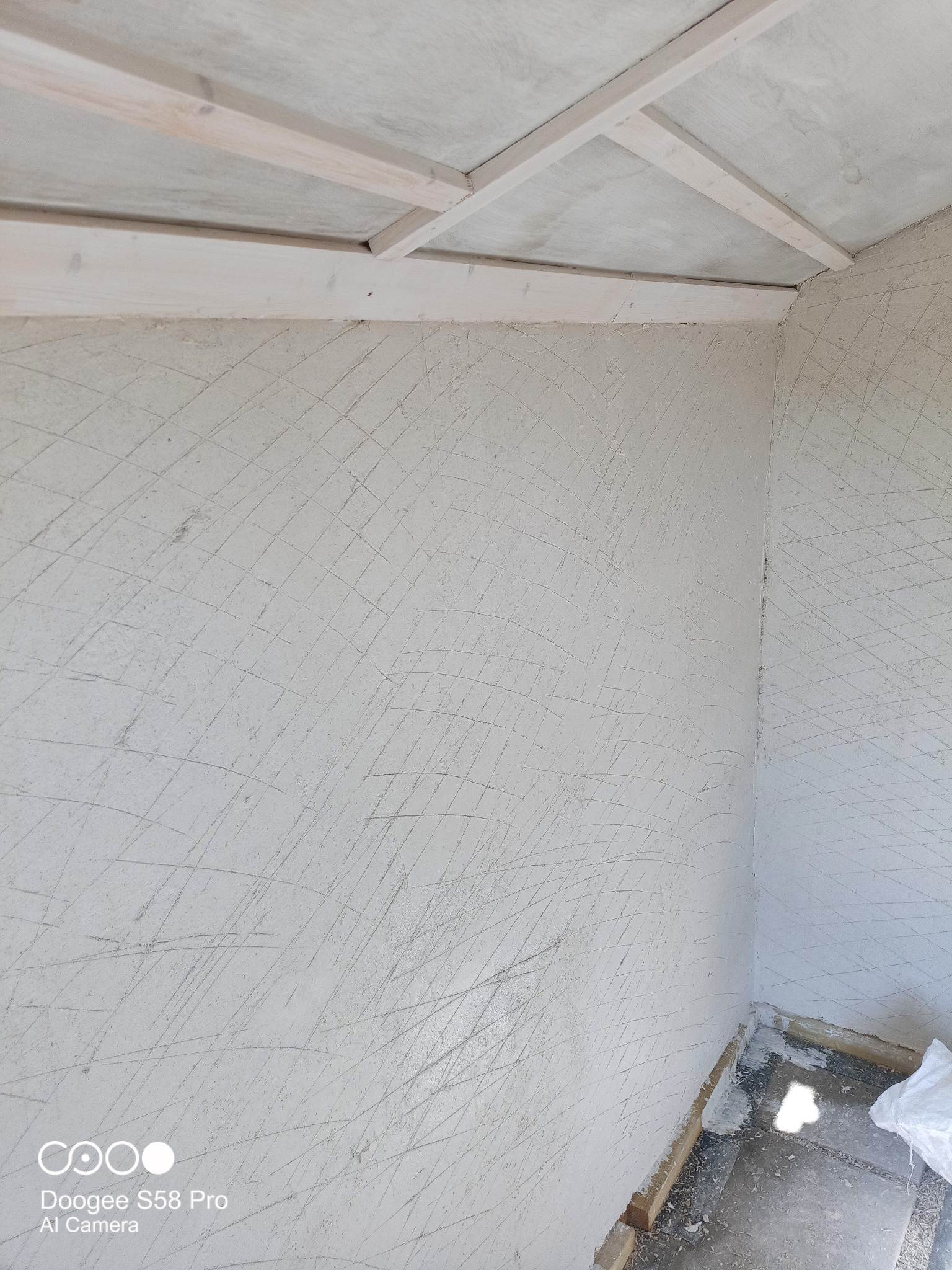 Wnętrze w trakcie prac przygotowawczych: surowy tynk z widocznymi śladami szpachli na ścianach i drewniana konstrukcja sufitu.