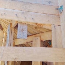 MAR- BUD - Surowa konstrukcja drewniana domu w trakcie budowy, widoczne deski, gwoździe i metalowe elementy mocujące.