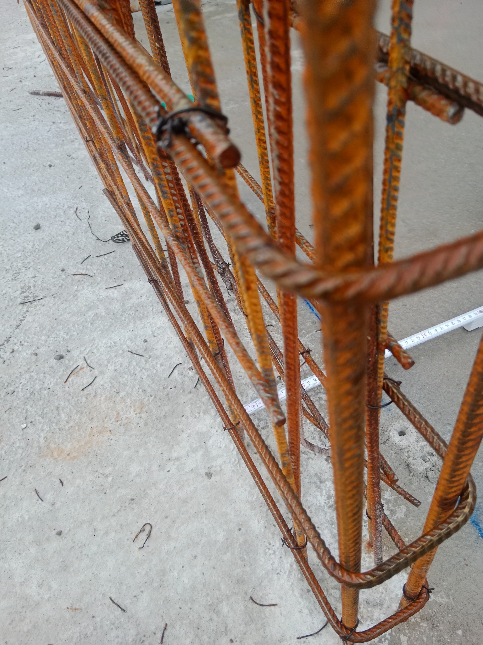 Zbrojenie fundamentowe z żebrowanych prętów stalowych, połączonych drutem wiązałkowym, widoczne na betonowej posadzce z rozrzuconymi resztkami drutu.