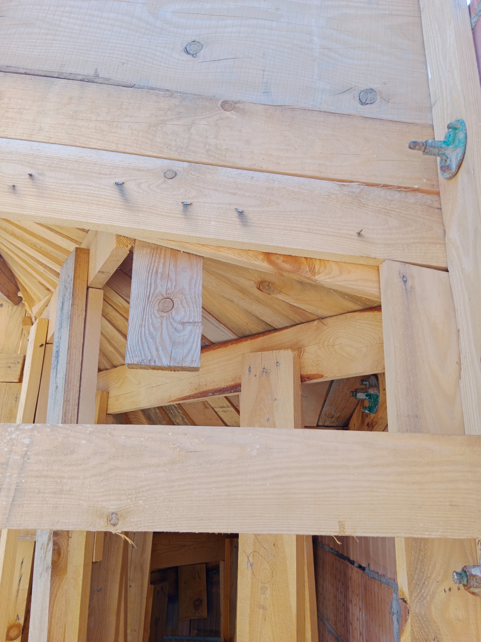 Surowa konstrukcja drewniana domu w trakcie budowy, widoczne deski, gwoździe i metalowe elementy mocujące.