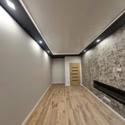 Pokój po remoncie z panelami podłogowymi, tapetą imitującą marmur, podwieszanym sufitem z oświetleniem LED i drewnianymi drzwiami.