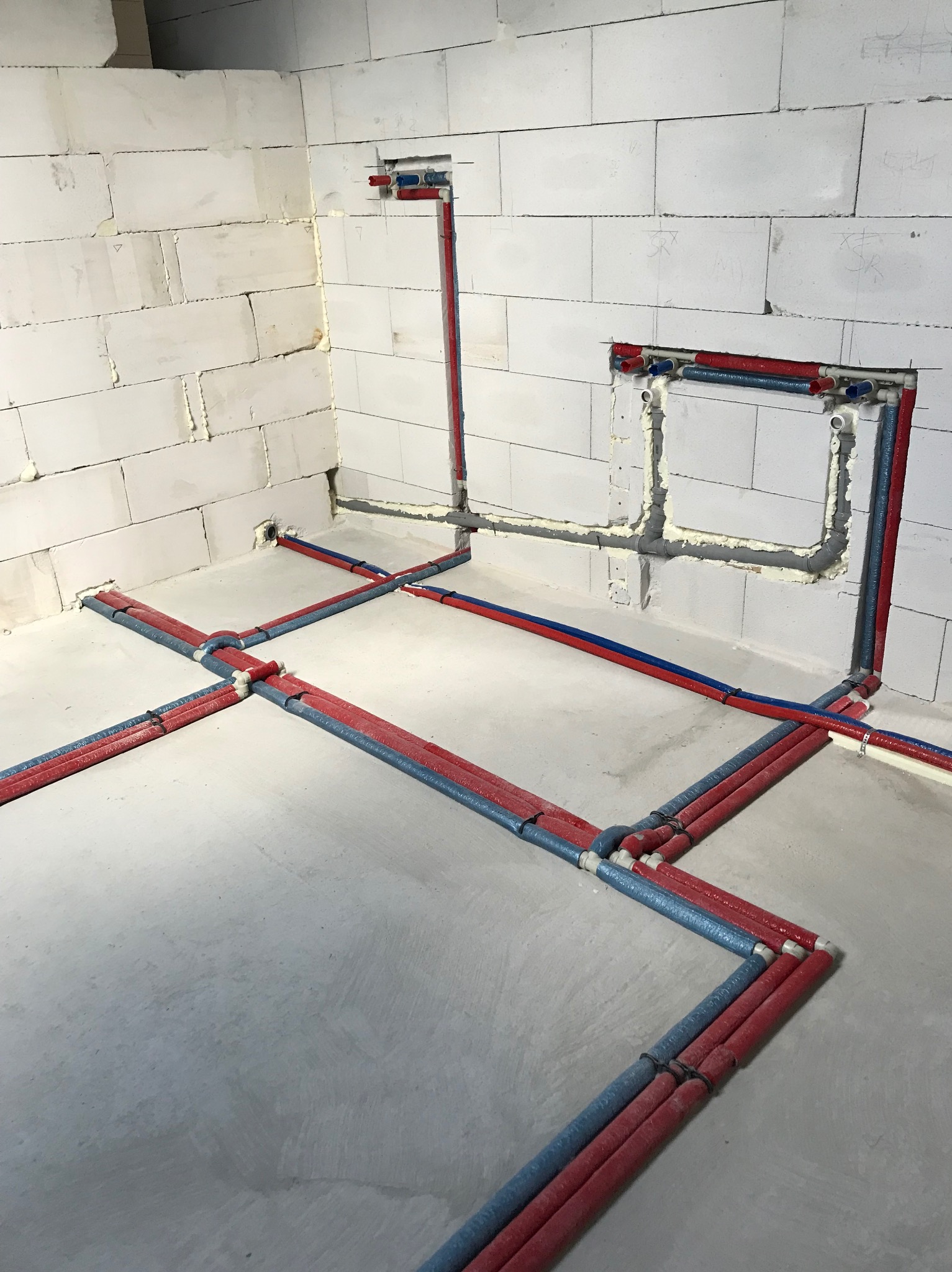 Instalacja wodna i grzewcza w surowym stanie budynku, rury czerwone i niebieskie prowadzone po podłodze i w ścianach z betonu komórkowego.