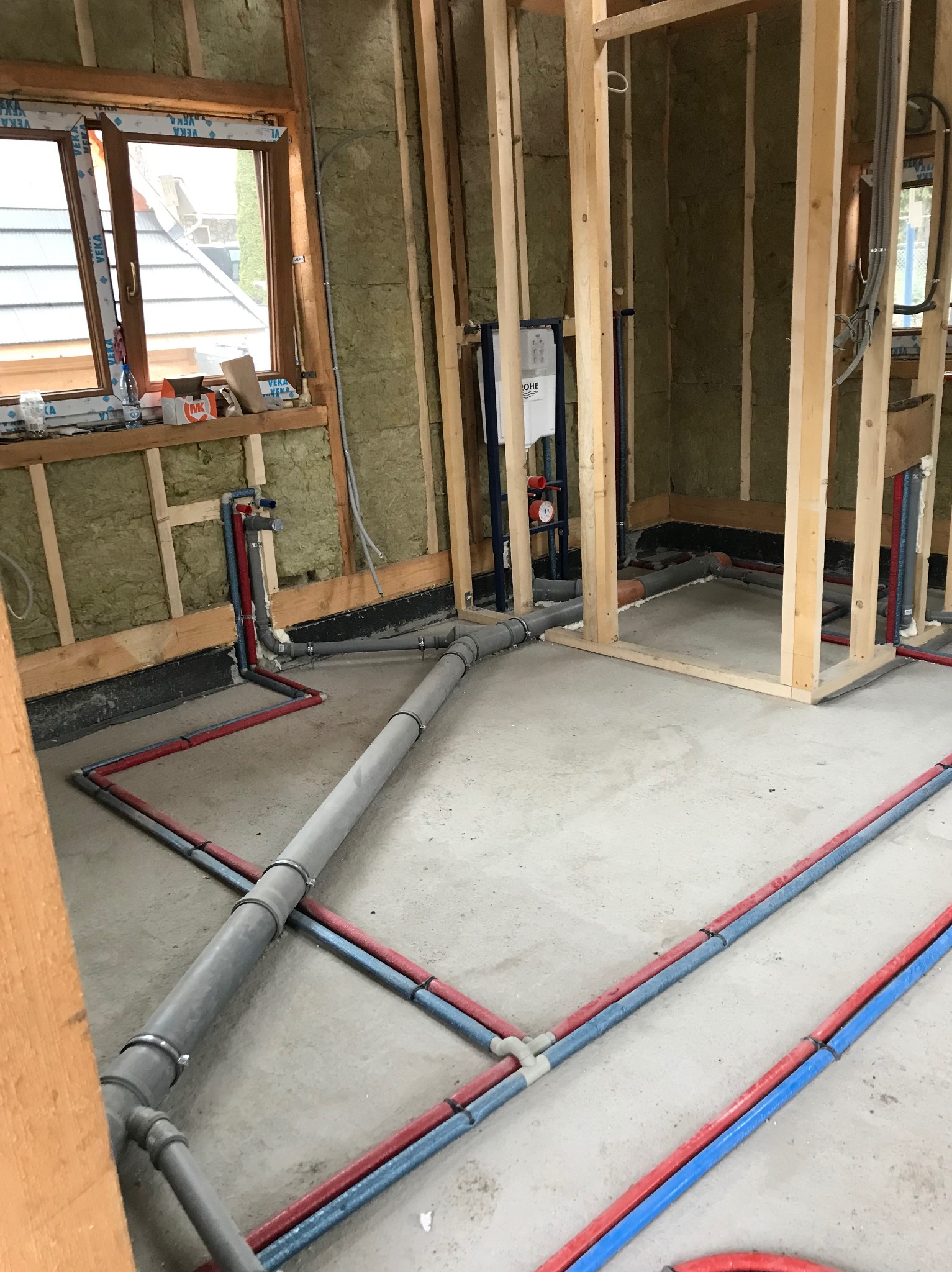 Surowy stan instalacji wodno-kanalizacyjnej w budynku w Czarnym Dunajcu, widoczne rury kanalizacyjne z szarego PCV, rury ciepłej i zimnej wody w izolacji czerwonej i niebieskiej, oraz stelaż...