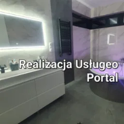 Nowoczesna łazienka z podświetlanym lustrem, grzejnikiem drabinkowym i okrągłą wanną z mozaiką, oświetlona fioletowym światłem.