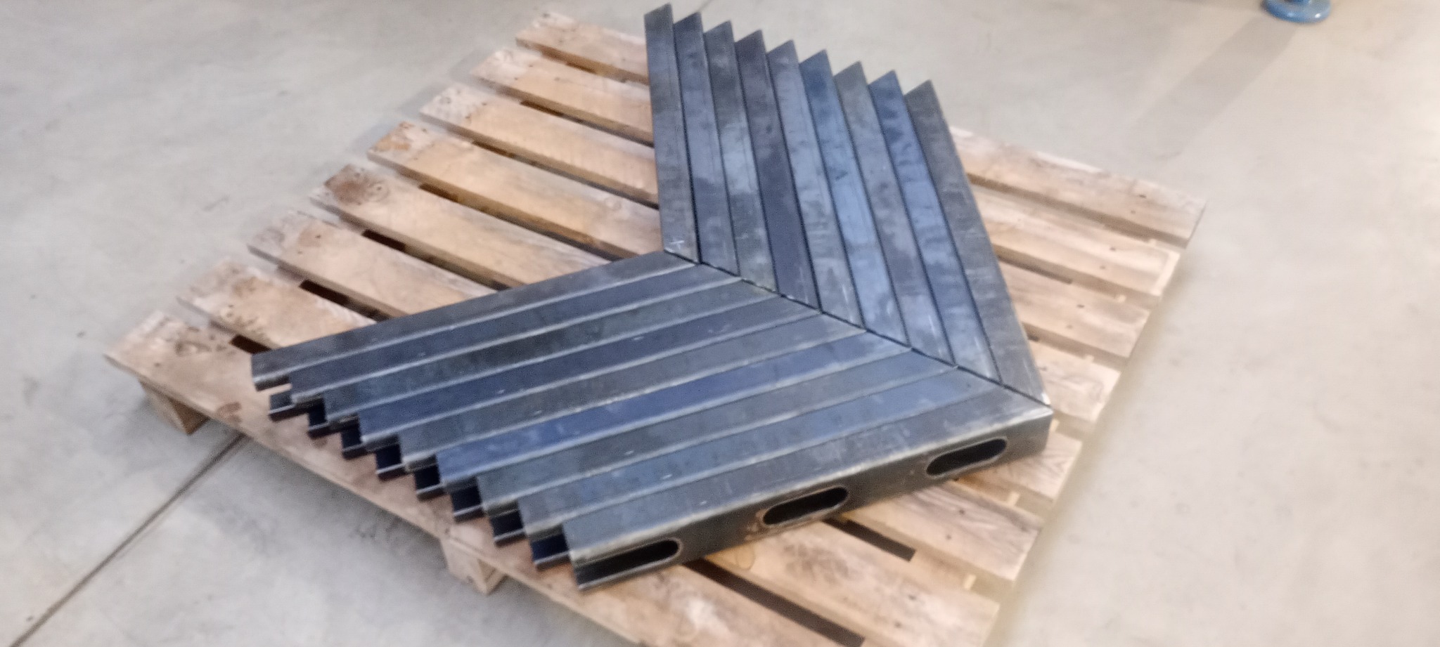 Szare, metalowe profile spawane pod kątem prostym, ułożone warstwami na drewnianej palecie.