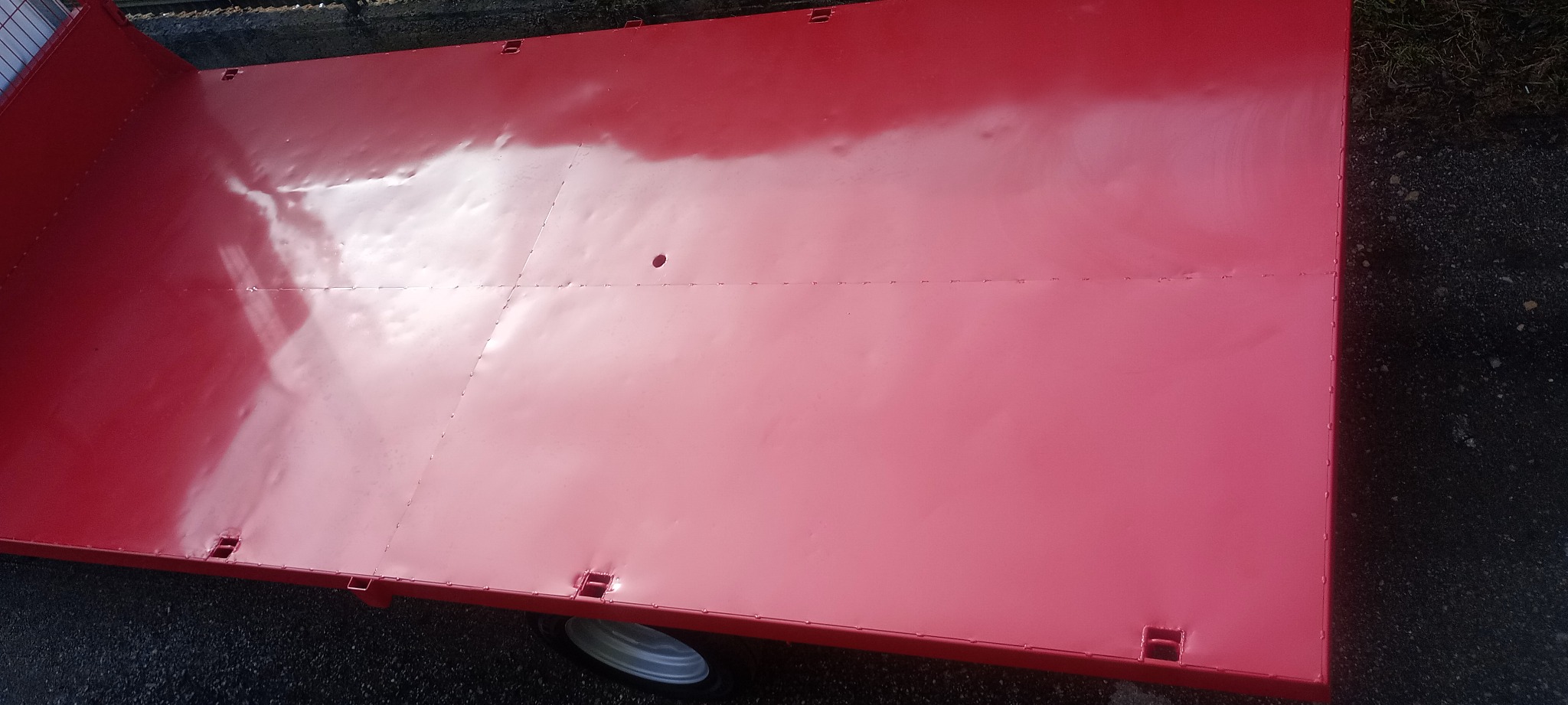 Czerwona, pomalowana i pospawana platforma przyczepy z widocznymi spawami i otworami montażowymi.
