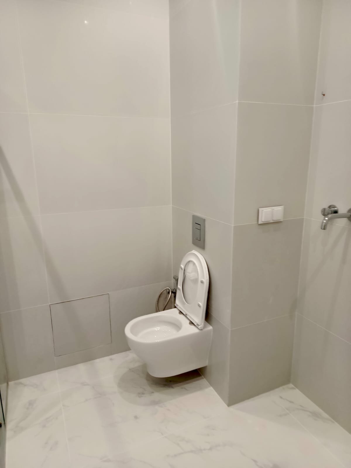 Nowoczesna, podwieszana toaleta w wyremontowanej łazience w Wałbrzychu. Białe płytki imitujące marmur na podłodze i ścianach. Minimalistyczny design.