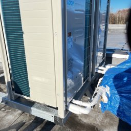 STAL-SPAW Karol Chwajoł - Dwa agregaty klimatyzacyjne VRV IV LOOP na dachu, z widocznymi rurami w izolacji i fragmentem niebieskiej plandeki. Metalowa konstrukcja wsporcza.