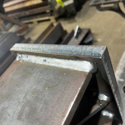 STAL-SPAW Karol Chwajoł - Precyzyjne spawy łączące metalowe elementy pod kątem, widoczne detale spoin i struktura metalu. Element konstrukcyjny w warsztacie.