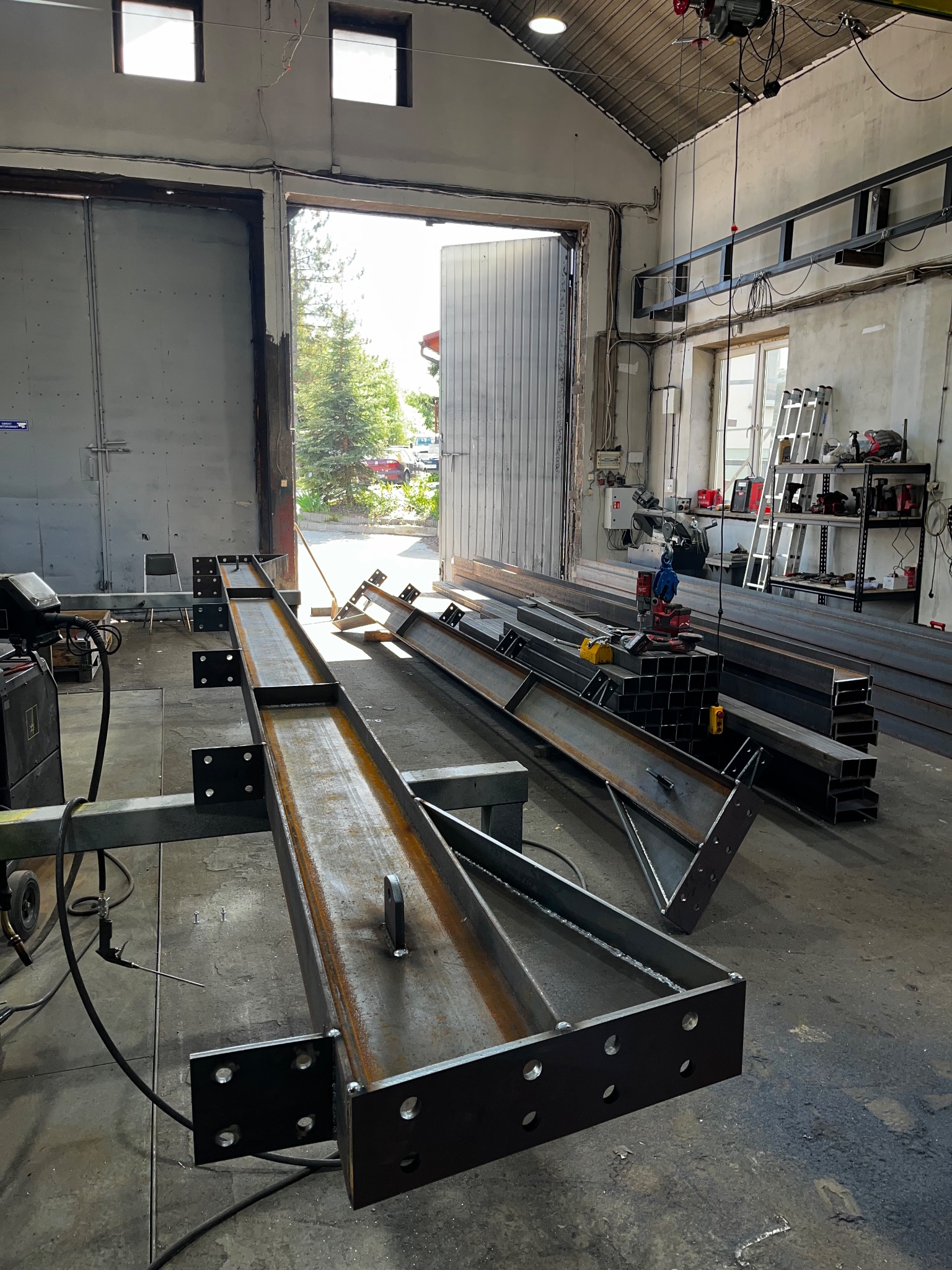 Przygotowane elementy stalowe z nawierconymi otworami i przyspawanymi mocowaniami, leżące w hali produkcyjnej, czekające na dalszy montaż.