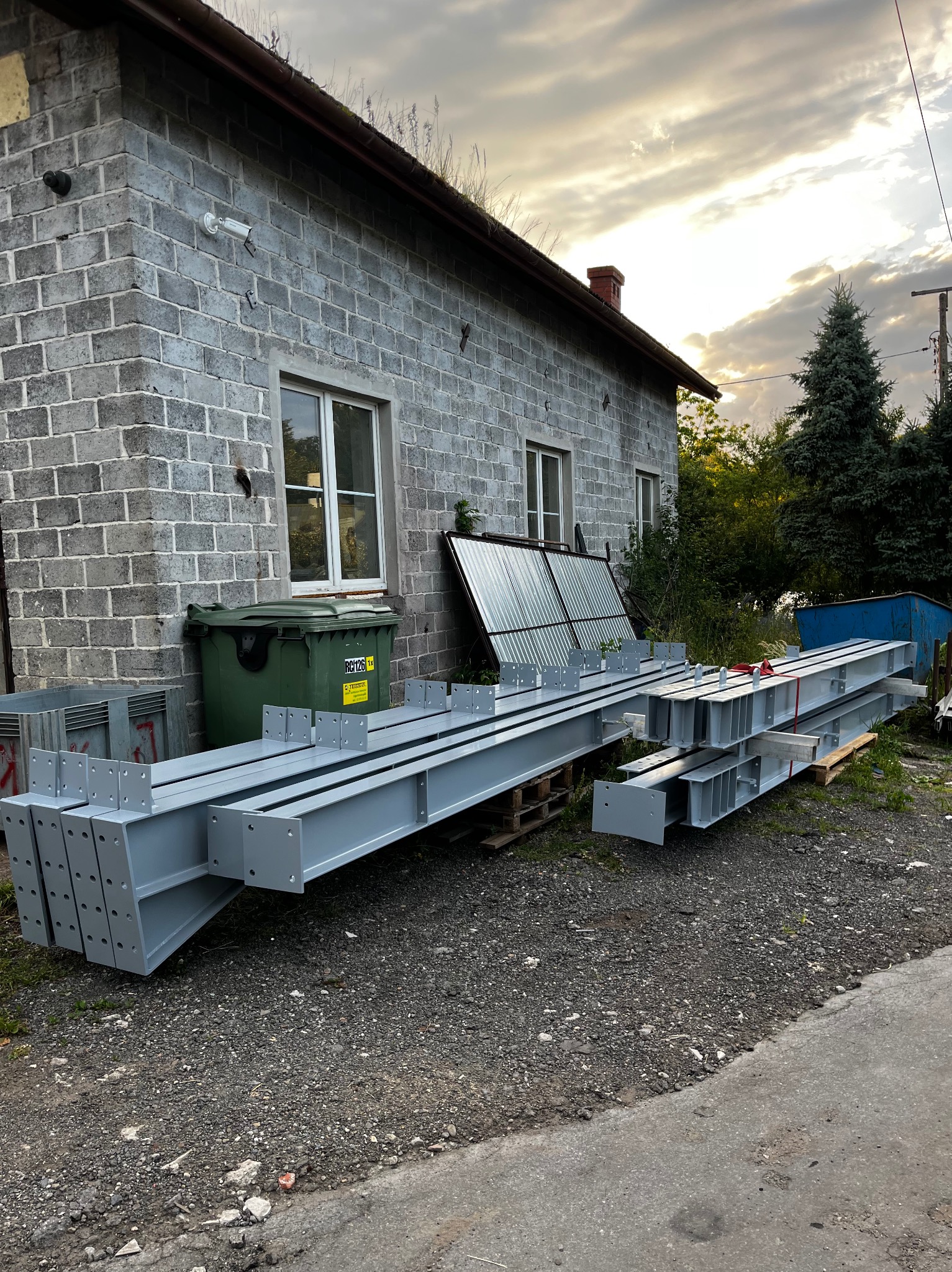 Gotowe, pomalowane elementy konstrukcji stalowej z otworami, ułożone na paletach przed budynkiem w Gdowie. Przygotowane do montażu.