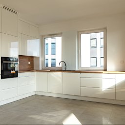 PRONEO SPÓŁKA Z OGRANICZONĄ ODPOWIEDZIALNOŚCIĄ - Jasna, nowoczesna kuchnia z białymi, lakierowanymi frontami, drewnianym blatem i wbudowanym piekarnikiem. Widok na okna z widokiem na budynek mieszkalny.