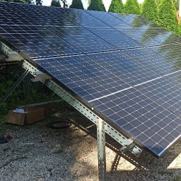 SABENERGY Sp. z O.O. - Panel słoneczny zamontowany na metalowej konstrukcji na tle zieleni, widoczne narzędzia i karton, instalacja w trakcie montażu.