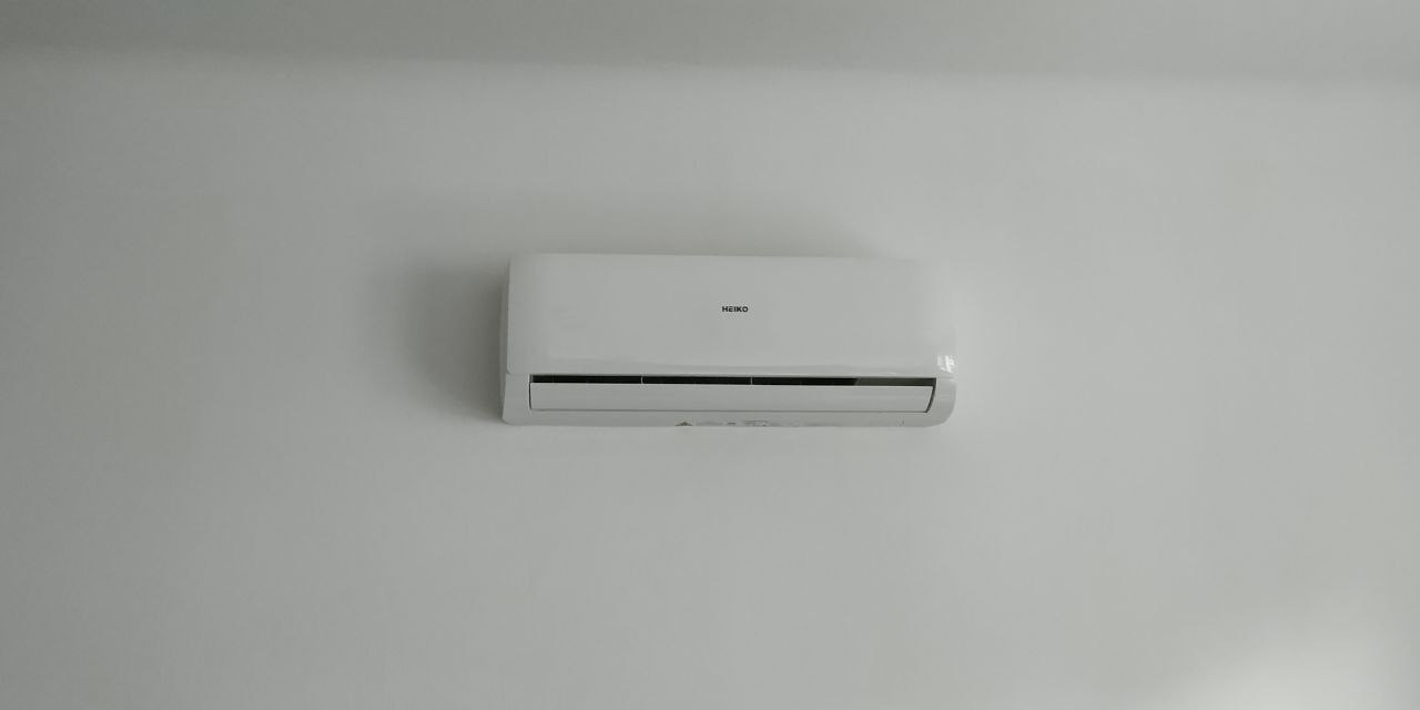 Biała klimatyzacja marki HEIKO zamontowana na jasnej ścianie, widoczna z przodu, z delikatnym cieniem na ścianie.