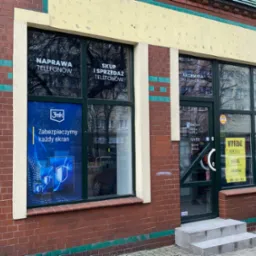 Fasada budynku z witrynami reklamującymi usługi: naprawa i skup telefonów, akcesoria do telefonów oraz moda męska. Na szybach naklejki z logo 3mk i informacją o zabezpieczaniu każdego ekranu.
