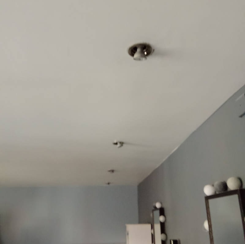 Rząd punktowych lamp sufitowych w szarym pokoju, widok z dołu. Oświetlenie wkomponowane w sufit, minimalistyczny design.