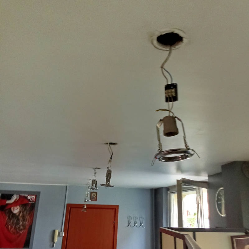 Niedokończony montaż oświetlenia sufitowego: wiszące przewody, puszka elektryczna i elementy lampy bez klosza w jasnym wnętrzu. Widoczne otwory w suficie.