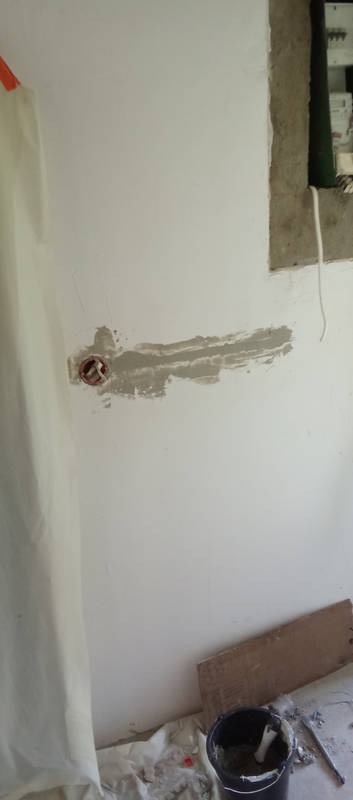 Przygotowanie ściany pod gniazdko elektryczne: zamaskowany otwór, szpachlowanie, widoczny fragment instalacji. Prace remontowe w trakcie wykańczania wnętrza.