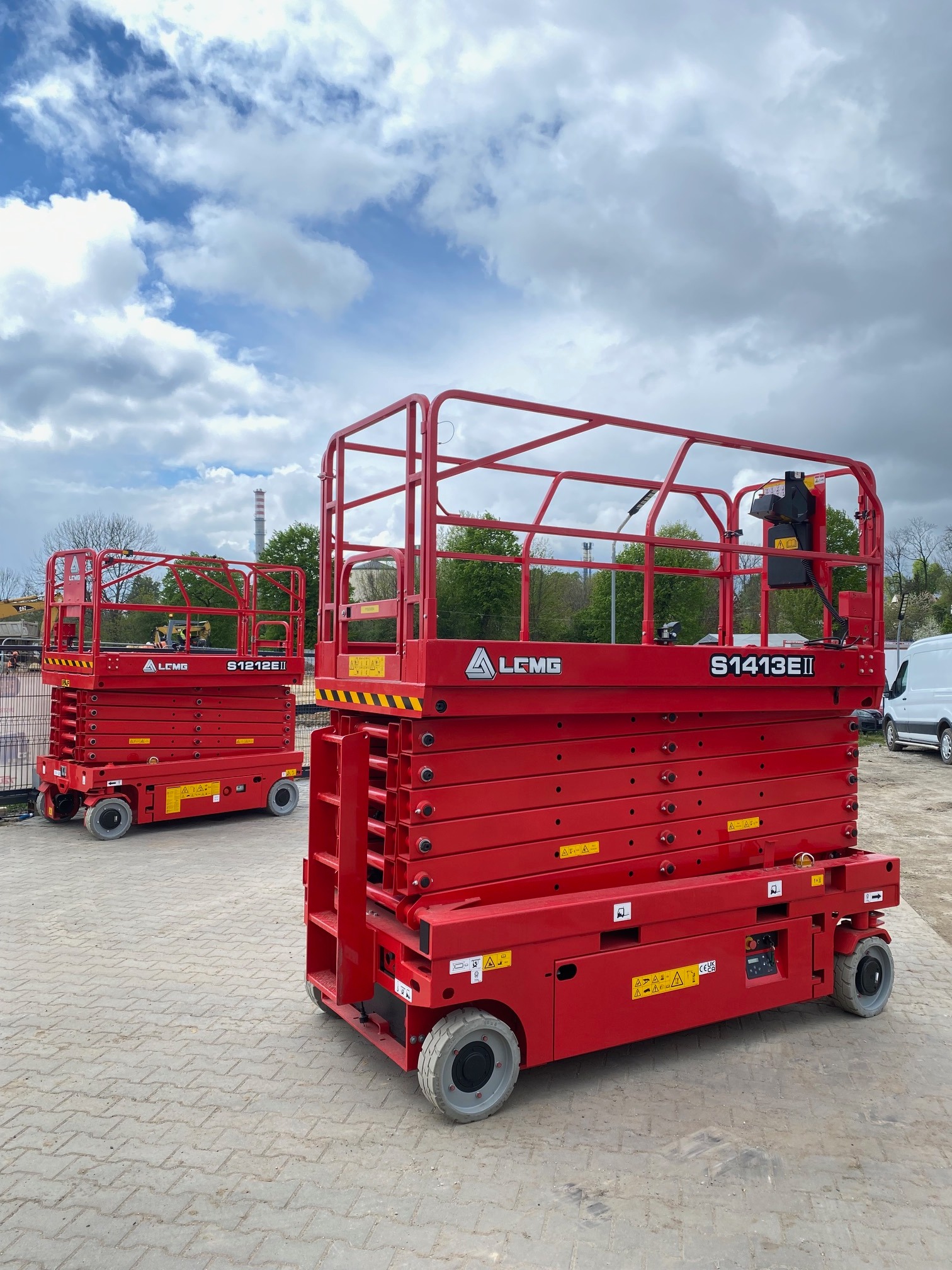 Dwie czerwone, nowe podnośniki nożycowe LGMG S1413EII i S1212EII na kostce brukowej, z błękitnym niebem w tle. Widoczne detale konstrukcyjne i oznaczenia.