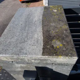 Fragment betonowej kostki brukowej, połowa wyczyszczona z mchu i zabrudzeń, widoczna różnica przed i po zabiegu, pomarańczowy samochód w tle.