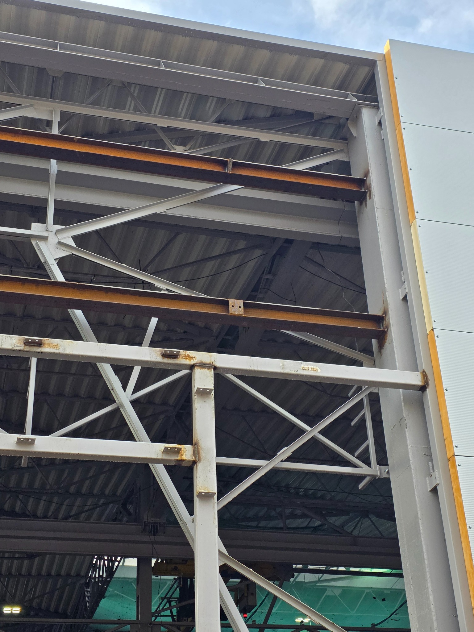 Konstrukcja stalowa hali przemysłowej w trakcie budowy, widoczne elementy nośne i obudowa. Detal z bliska, zardzewiałe elementy.