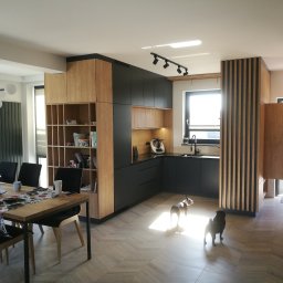 Stolarstwo - Nowoczesna kuchnia z czarnymi szafkami i drewnianymi akcentami, oświetlona światłem dziennym, z dwoma psami na parkiecie ułożonym we wzór jodełki.