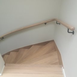 Stolarstwo Witbrodt Sławomir - Drewniane schody z jasnego drewna z zamontowaną poręczą z naturalnego drewna i czarnymi uchwytami, widok z góry, minimalistyczny design.