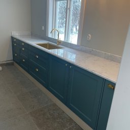 Stolarstwo - Elegancka zabudowa kuchenna w odcieniach zieleni z marmurowym blatem i złotą armaturą, Wejherowo. Widok na okno z zimowym krajobrazem.