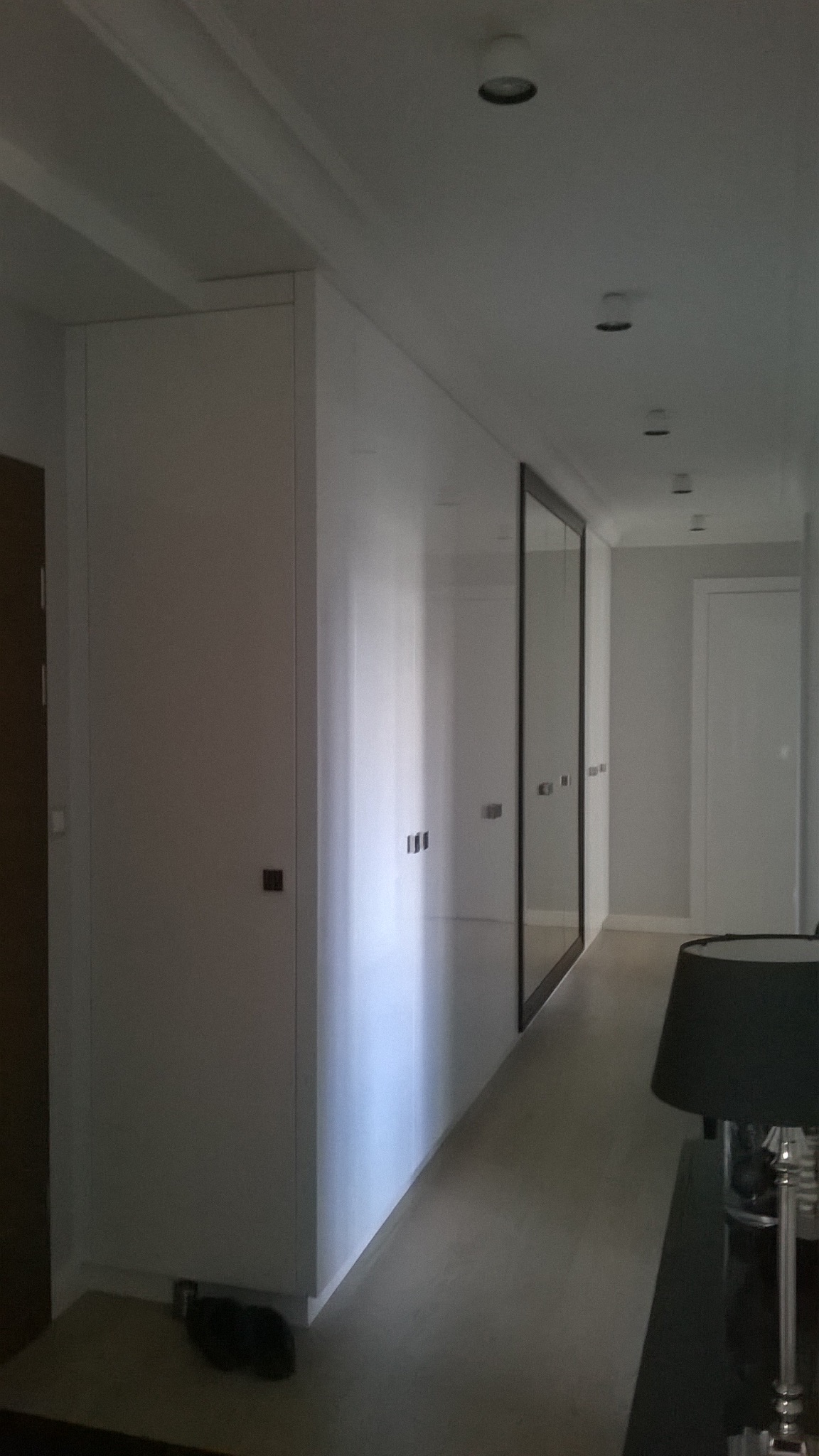Długa, biała szafa wnękowa z lustrzanymi drzwiami w korytarzu, minimalistyczny design, oświetlenie punktowe, widok z perspektywy.
