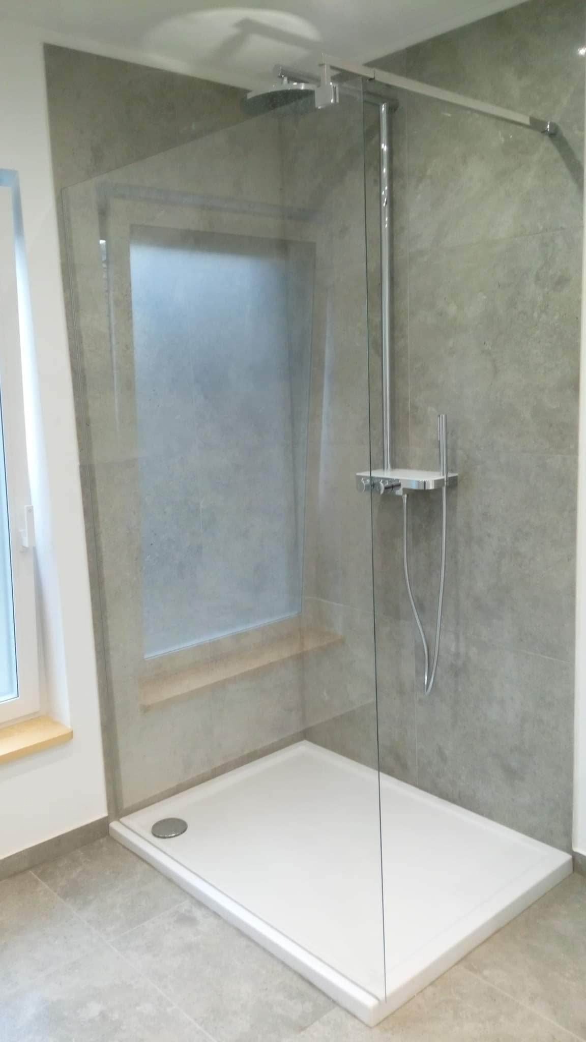 Nowoczesna kabina prysznicowa walk-in z szarą płytką imitującą kamień, biały brodzik i chromowana armatura, widok z boku na ukończoną łazienkę z oknem.