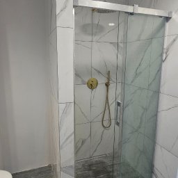 Alex Oleksandr Lisovyi - Nowoczesna kabina prysznicowa ze złotą armaturą i przesuwnymi drzwiami, wykończona płytkami imitującymi marmur na ścianach i płytkami imitującymi drewno na podłodze, widoczne ślady po remoncie.