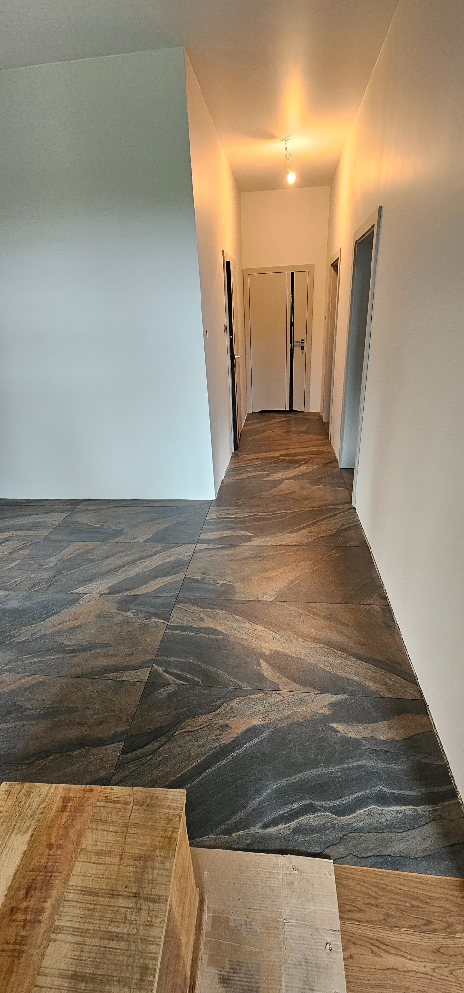 Położone płytki podłogowe imitujące kamień w korytarzu z widocznymi drzwiami po obu stronach, ciepłe oświetlenie sufitowe.